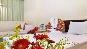 A hotel room with a bed, pillows, a bedside table, and a vase of flowers.