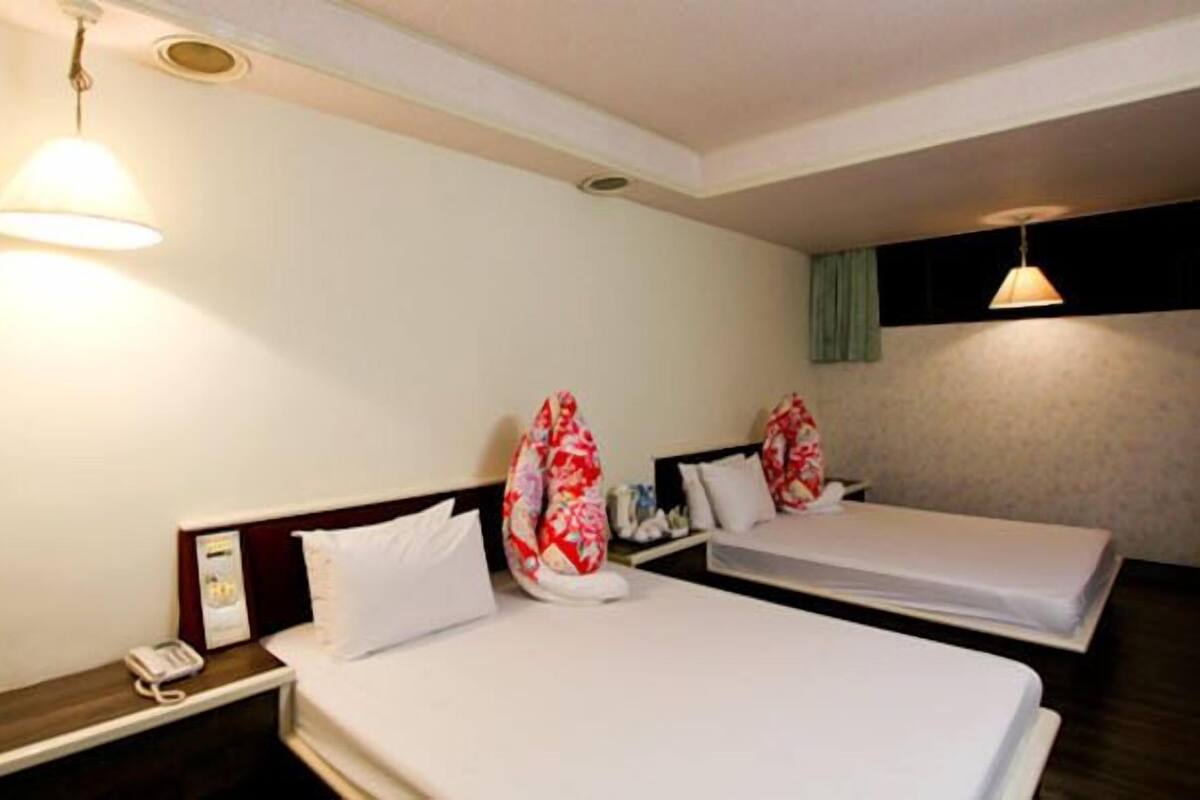 Una habitación de hotel con dos camas individuales, una mesita de noche con teléfono y una lámpara de pared.