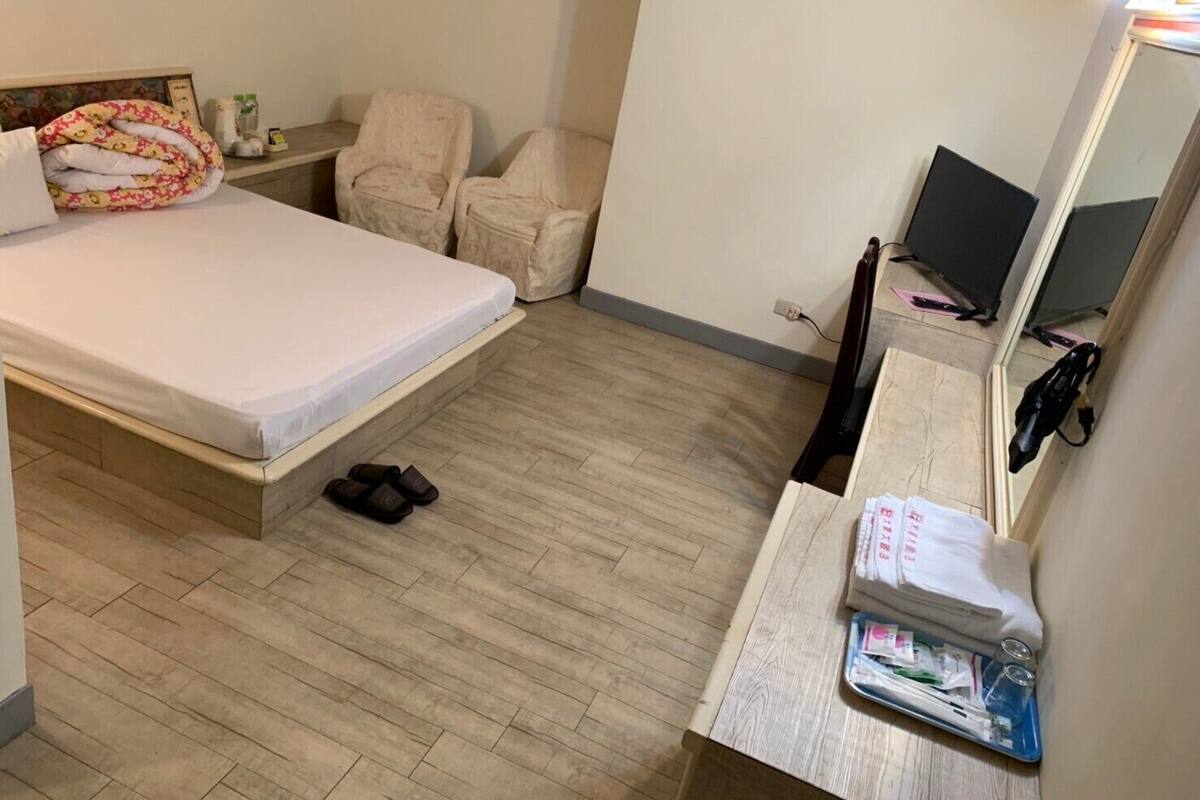 Un dormitorio pequeño y ordenado con cama, una silla, un escritorio con espejo y una computadora portátil.