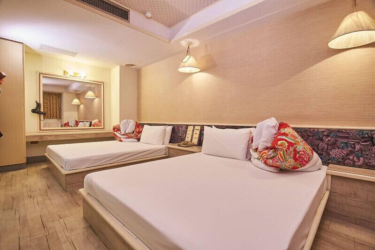Una habitación de hotel con dos camas, un espejo grande y un cabecero de madera.