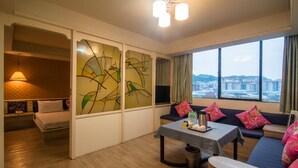 A hotel room with a bed, a sofa, a table with amenities, a city view, and abstract art on the wall. - Dahua Hotel (Keelung)