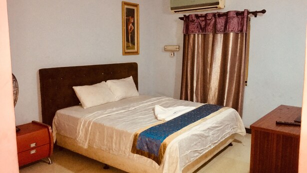 Une chambre à coucher comprenant un lit, une table de chevet, une commode, un climatiseur et un rideau.