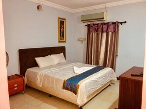 A bedroom with a bed, a nightstand, a dresser, an air conditioner, and a curtain.