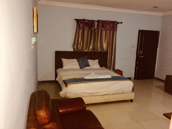 A bedroom with a bed, a nightstand, a brown leather sofa, a door, and a wall-mounted light fixture.