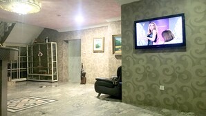 Un salon avec un téléviseur fixé au mur, un lustre, un canapé en cuir noir et un papier peint à motifs.