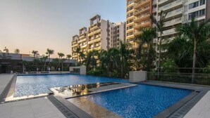 Zona de piscina con solárium de baldosas, rodeada de palmeras y modernos edificios de apartamentos.