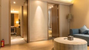Una habitación de hotel moderna con una mesa de centro redonda, un sofá y una lámpara. Tiene pisos de madera y una puerta que da a otra habitación.