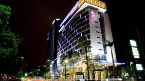 Un hotel moderno con una fachada de vidrio destacada, varios pisos y una terraza en la azotea.