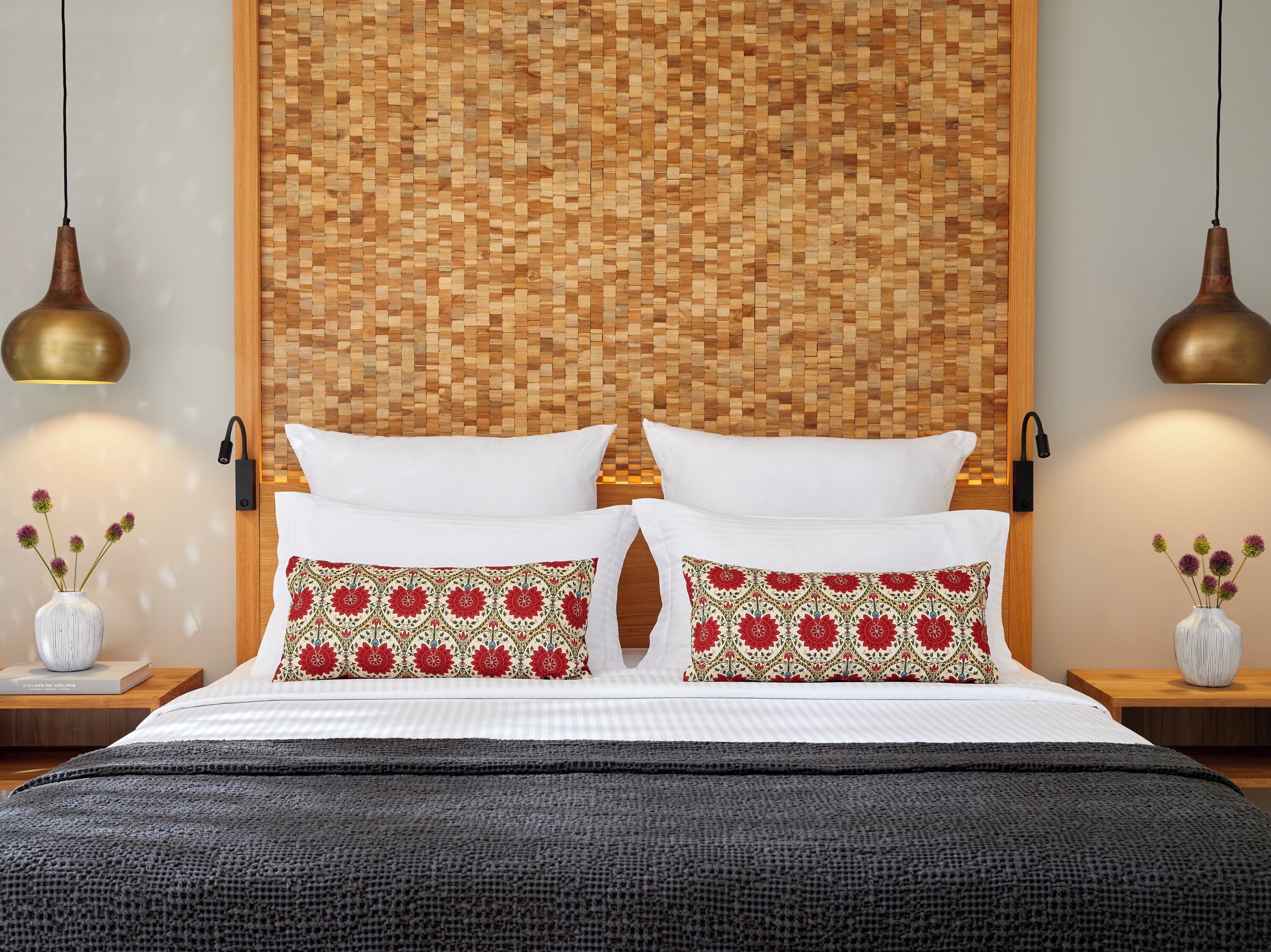 A neatly made bed with white bedding and two decorative pillows, a woven headboard, and two wall-mounted lamps.