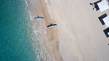 An aerial view of a beach with two paddleboards and a row of beach chairs and umbrellas.