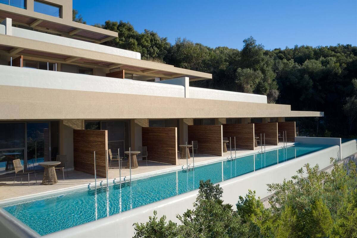 Un edificio moderno con piscina, mobiliario exterior y vistas al bosque circundante.