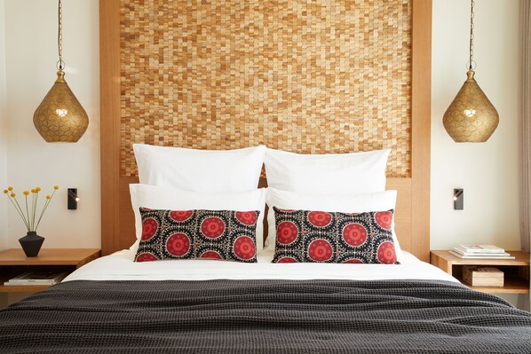 A neatly made bed with white and patterned pillows, a woven headboard, and two hanging lamps.