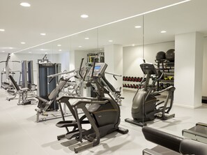 A modern gym with various exercise equipment, including treadmills and weight machines, and a rack of dumbbells.