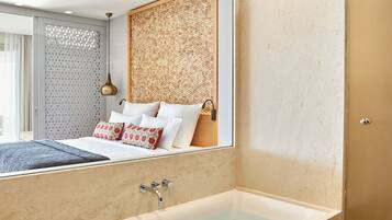Un baño moderno con bañera, un espejo grande y una cama con almohadas blancas y rojas.