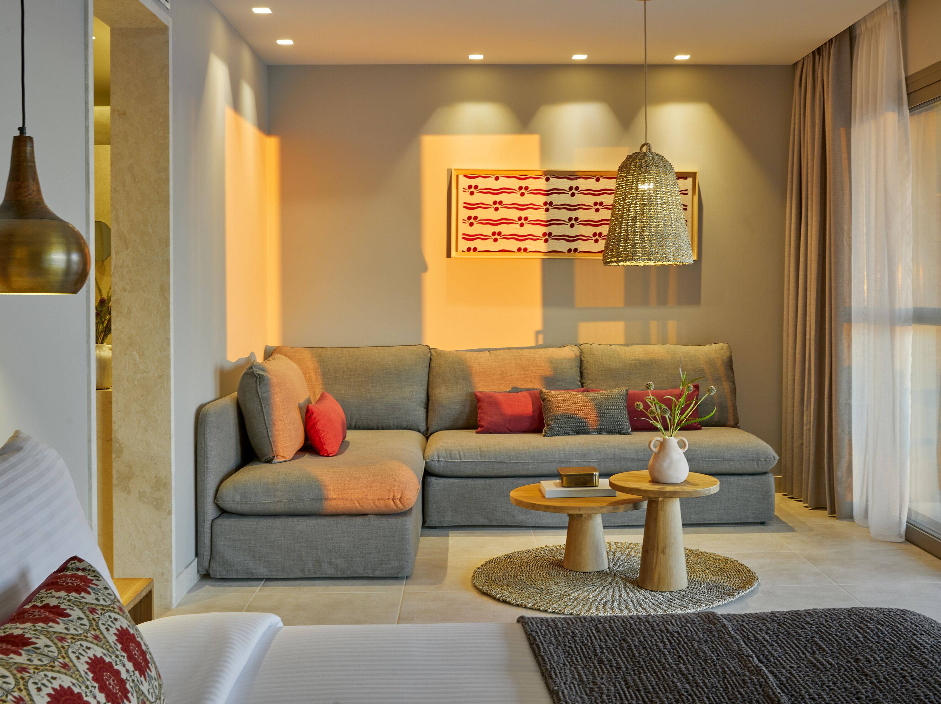 A modern living room with a grey sofa, red and grey cushions, a wooden coffee table, and a hanging light fixture.