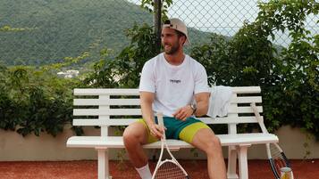 A person sitting on a white bench with tennis rackets and balls beside them.