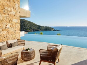 A terrace with a stone wall, wicker furniture, and a view of the sea.