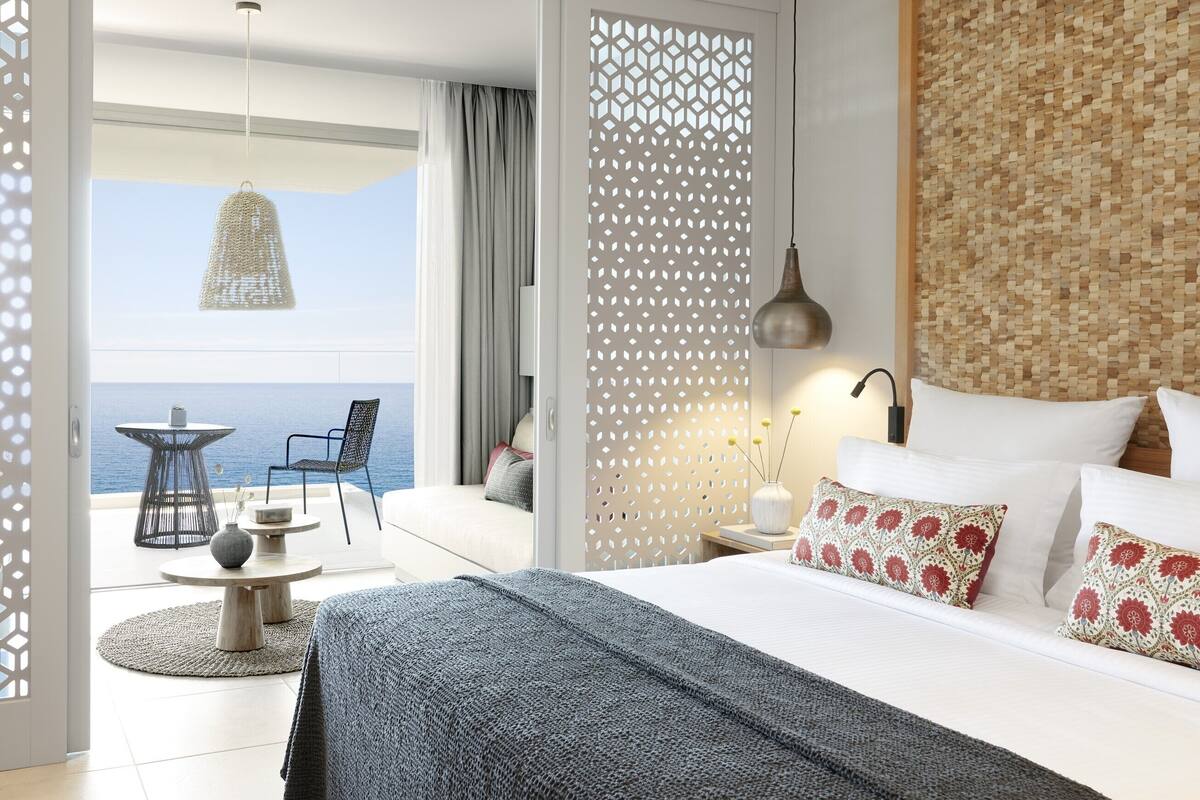 Una habitación de hotel moderna con una cama grande, un balcón con vistas al mar, un comedor y una pared decorativa.