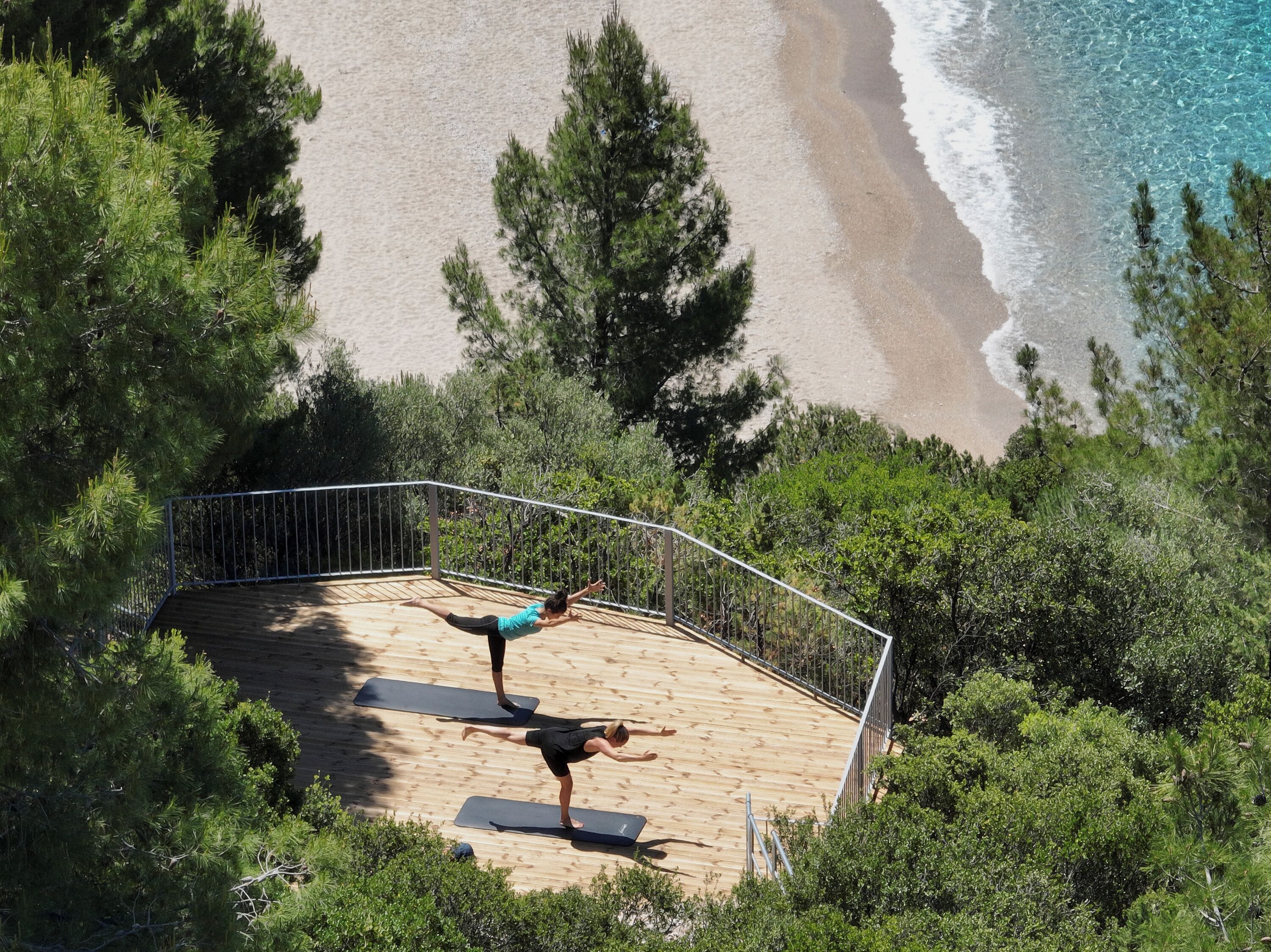 A wooden deck with two yoga mats, overlooking a beach and ocean.