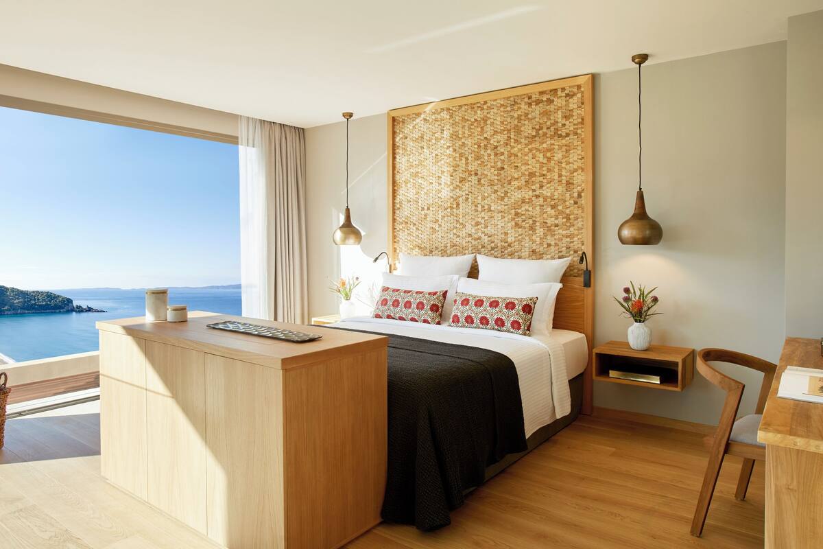 Una habitación de hotel moderna con una cama grande, un escritorio de madera y vista al mar.