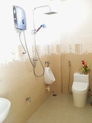 Un baño con orinal, inodoro y cabezal de ducha empotrado en la pared.