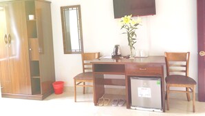 Une pièce comprenant un bureau en bois, deux chaises, un petit réfrigérateur, un vase avec des fleurs, une poubelle rouge et une armoire.
