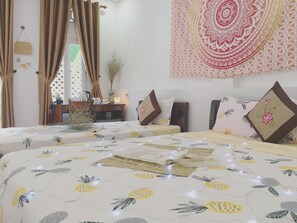 Una habitación de hotel con dos camas, cada una con una colcha de motivos florales, una mesita de noche con lámpara y un tapiz en la pared.