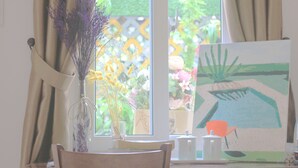 Une pièce avec une fenêtre, un vase contenant des fleurs séchées, un tableau accroché au mur et une chaise.