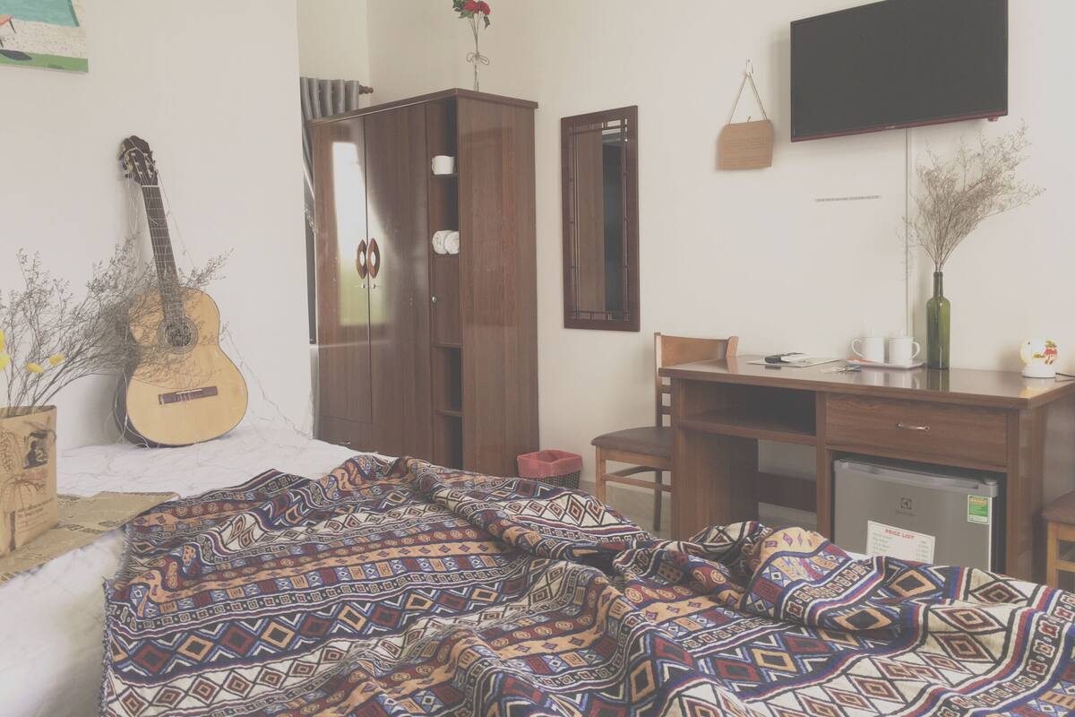 A bedroom with a bed, a desk, a chair, a television, and a guitar.