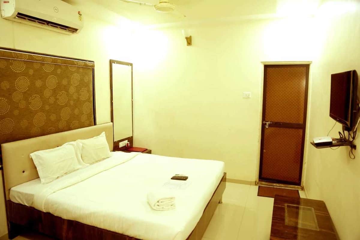 Habitación de hotel con cama, televisor montado en la pared, equipo de aire acondicionado y una puerta con mosquitera.