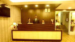 A reception area with a wooden reception desk, a flat-screen TV mounted on the wall, and a staircase leading to an upper floor. - Pan Club Hotel (Vapi)