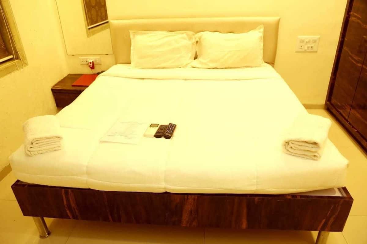 Una habitación de hotel con una cama, dos almohadas, una mesita de noche con un libro rojo y un control remoto.