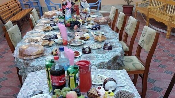 A long dining table set with various foods and drinks, surrounded by chairs. - Nozisayyoh (Bukhara)
