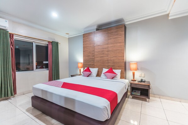 Habitación de hotel con una cama grande, dos mesitas de noche, una ventana con cortinas y un cabecero de madera.