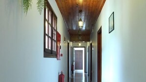 Un pasillo largo y estrecho con vigas de madera en el techo, un extintor y una planta colgante.
