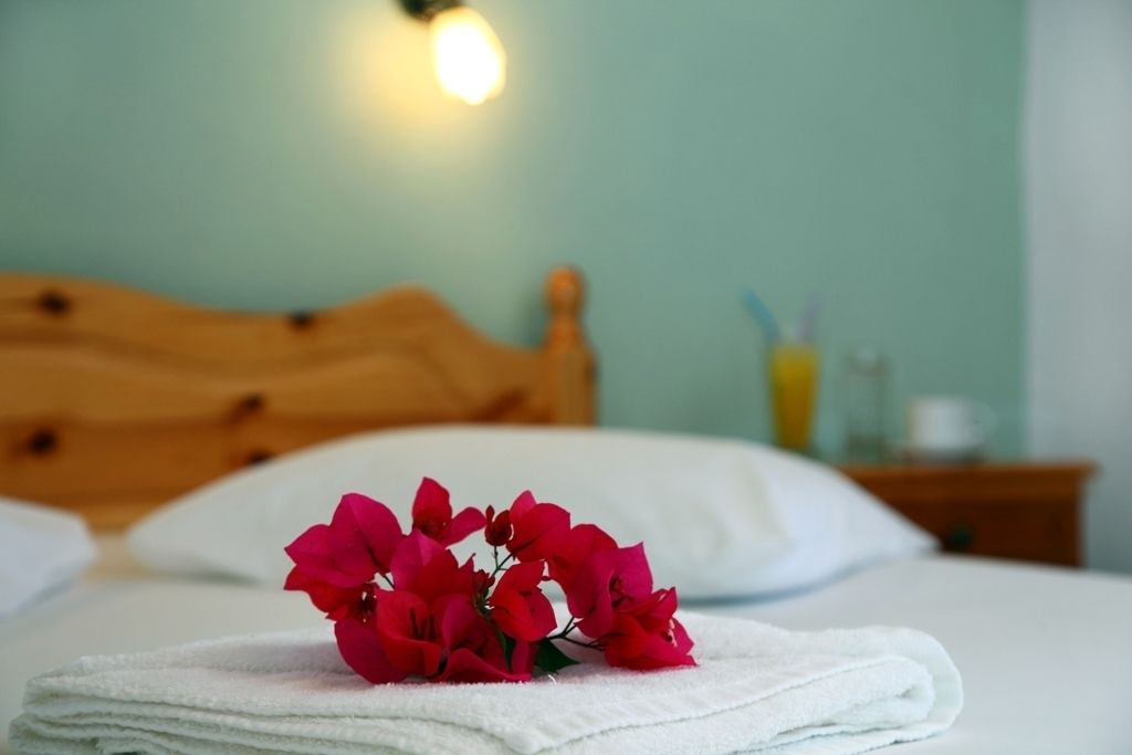A neatly made bed with a white towel and a bouquet of red flowers on top.