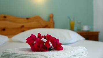 A neatly made bed with a white towel and a bouquet of red flowers on top.