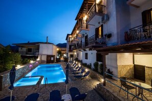 Un espace piscine doté de chaises longues et d’un bar, entouré d’immeubles avec des balcons et un éclairage extérieur.