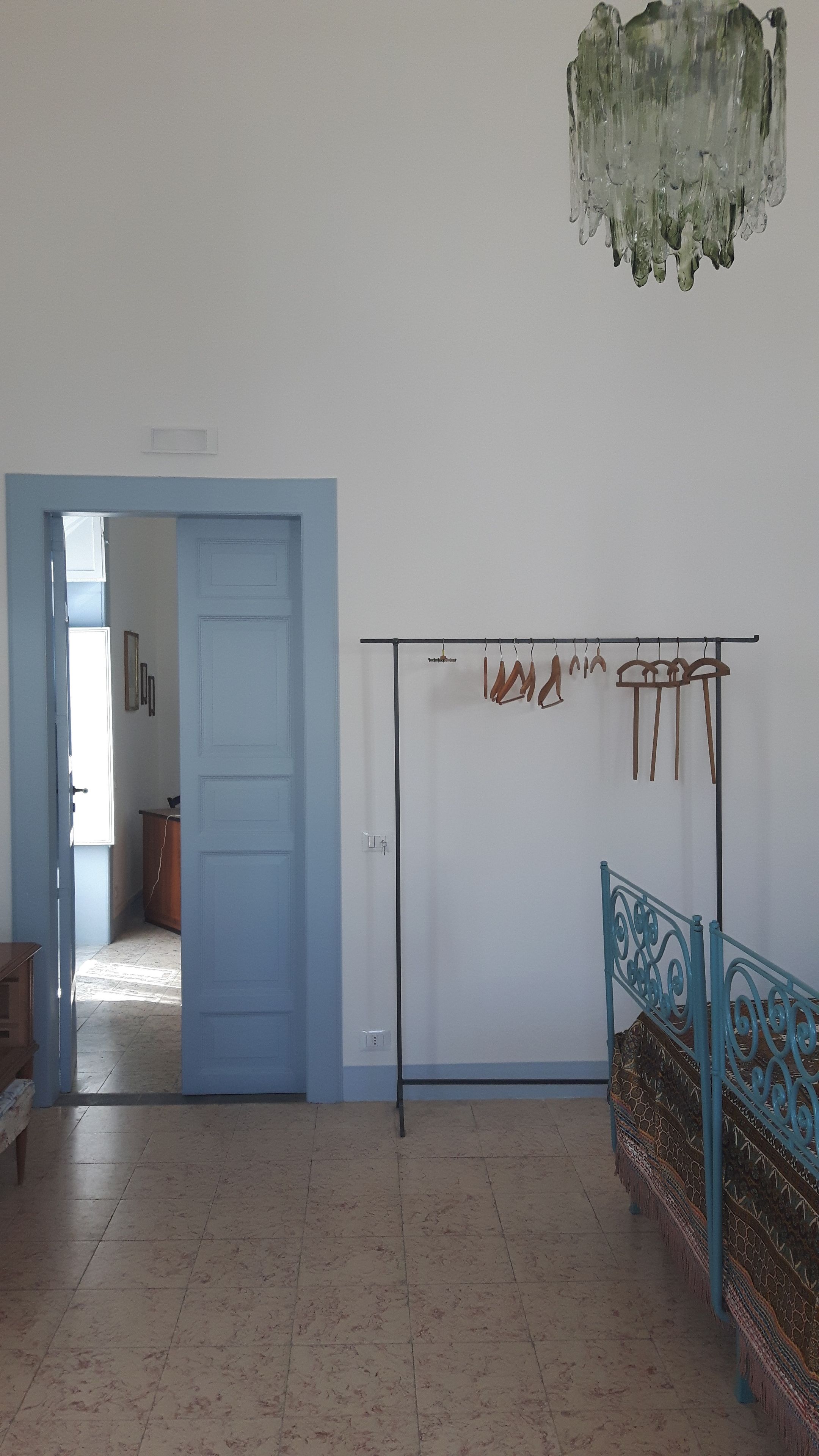 A room with a blue door, a hanging clothes rack, a patterned sofa, and a chandelier.