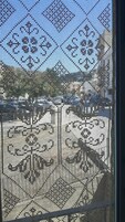 Vista a través de una ventana con un celosía decorativa, mostrando un estacionamiento y edificios al fondo.