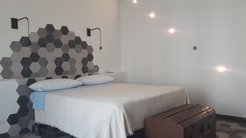 Una camera da letto con un letto, cuscini, un comodino, una panca di legno, una parete rivestita di piastrelle esagonali e luci a parete.
