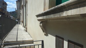 A narrow urban street with a stone pathway leading to a building with classical architecture, including a balustrade and decorative moldings. - Casa Maltese ri Scicli (Scicli)