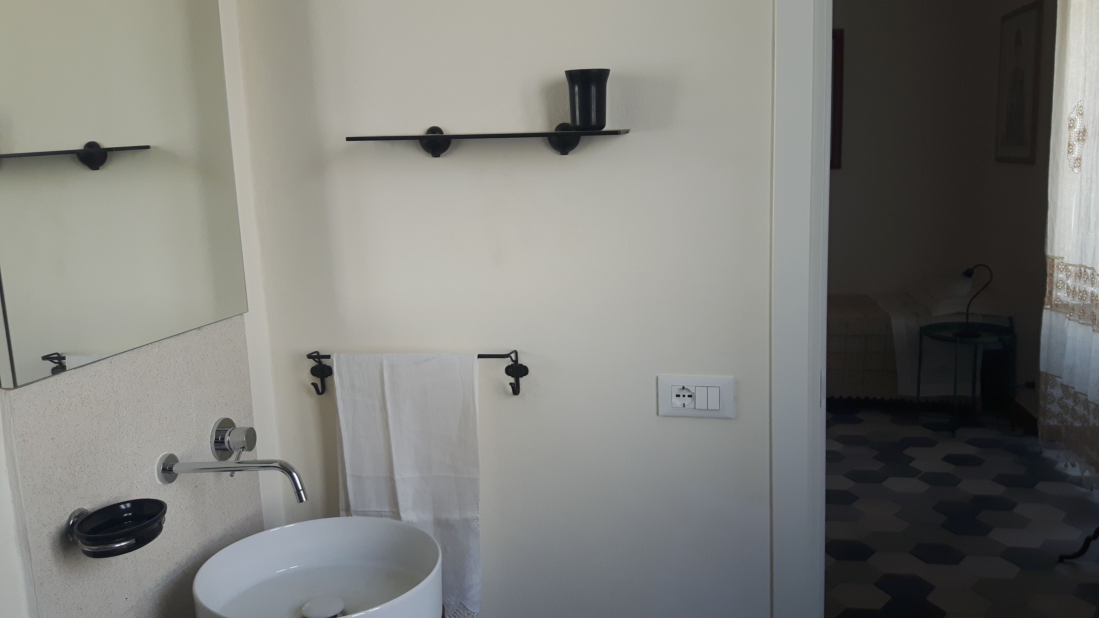 A bathroom with a white sink, a mirror, a towel rack, and a shelf with a cup.