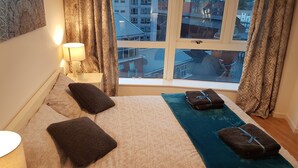 Hotellihuone, jossa on sänky, tyynyjä, yöpöytälamppu ja ikkunasta avautuva näkymä kaupunkiin.
