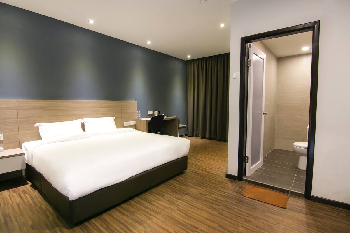 Una habitación de hotel moderna con una cama grande, un escritorio y zona de ducha.