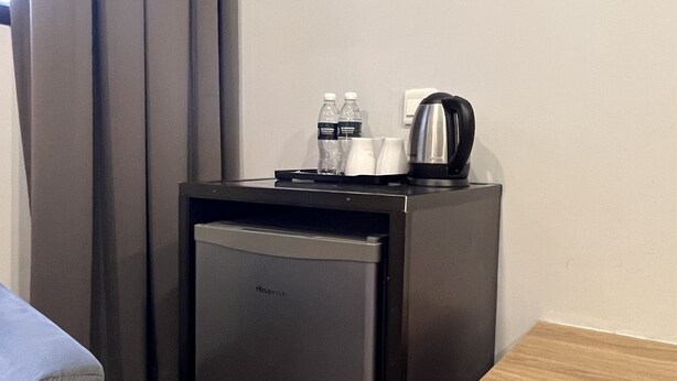 Une petite cuisine équipée d’un réfrigérateur, d’une machine à café et de deux bouteilles d’eau.
