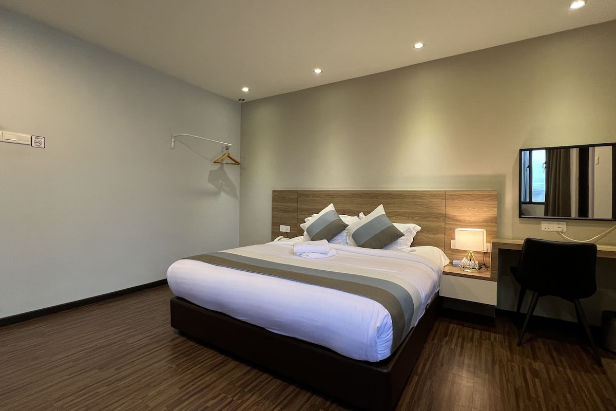 Una habitación de hotel con una cama grande, mesitas de noche, un escritorio con una silla y un televisor de pantalla plana montado en la pared.