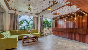 A spacious living room with a green sofa, wooden coffee table, and a ceiling fan. - Vijaygarh Resort & Cottages with Private Pool (Udaipur)