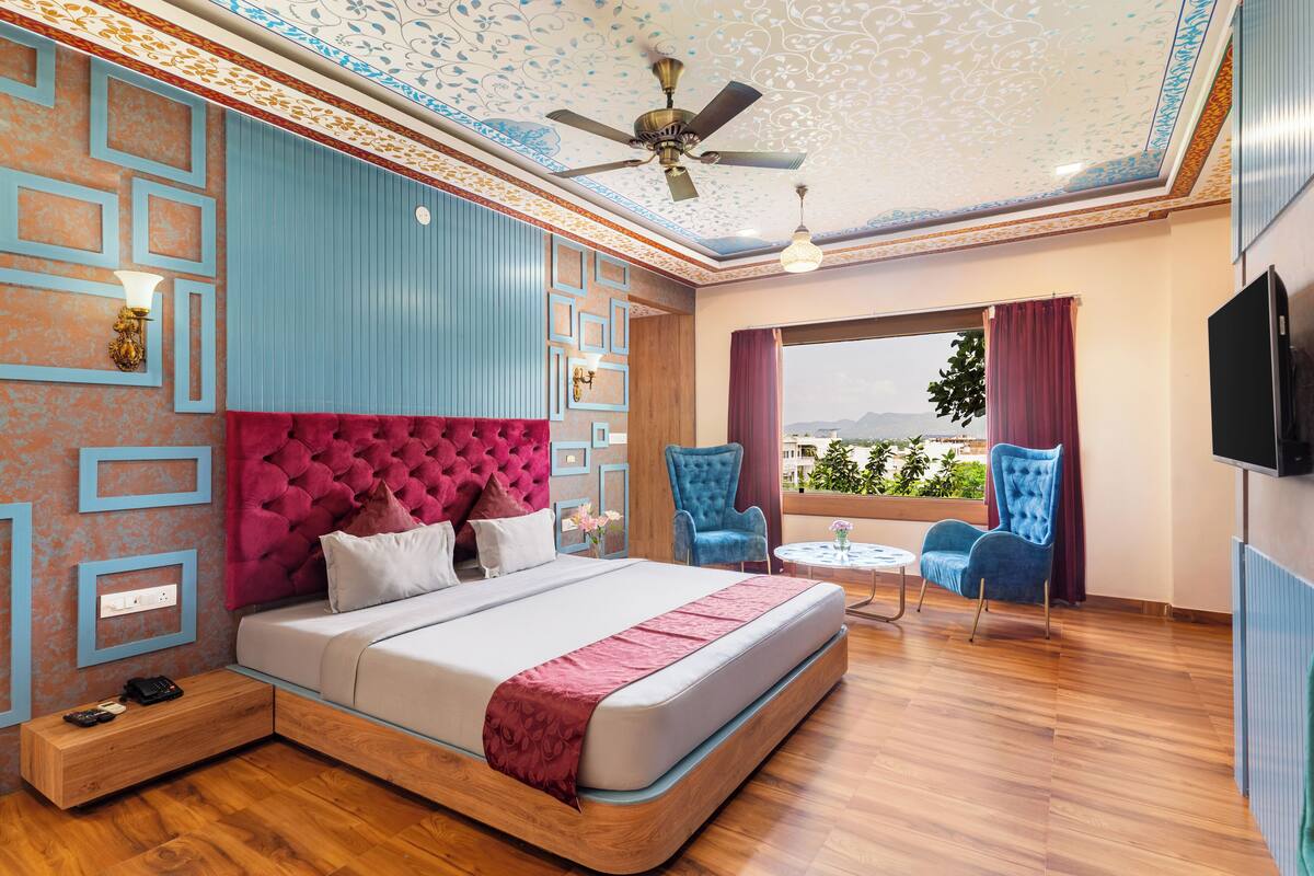 A bedroom with a bed, a ceiling fan, a TV, and a window with a view.