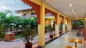A covered outdoor area with potted plants, a tiled floor, and wooden tables and chairs. - Vijaygarh Resort & Cottages with Private Pool (Udaipur)